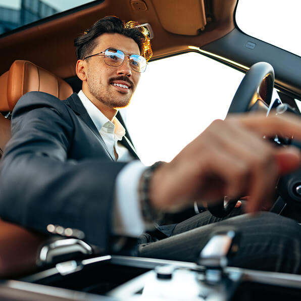 Driver in a suit inside a car with brown leather seats.