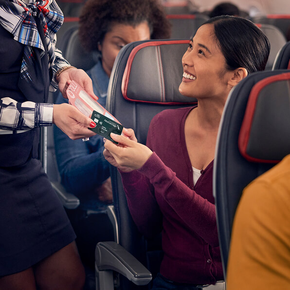 A smiling, seated passenger passes a Globe™ credit card to an attendant in an airplane cabin.