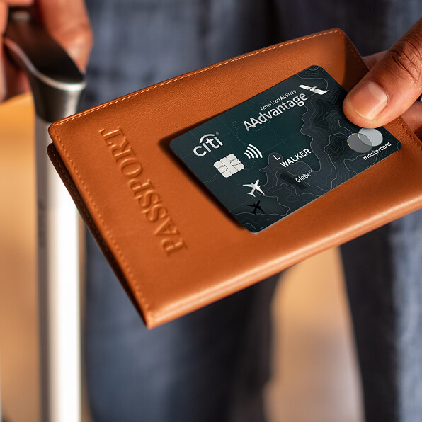 Traveler holding a Globe™ credit card, passport and suitcase handle.