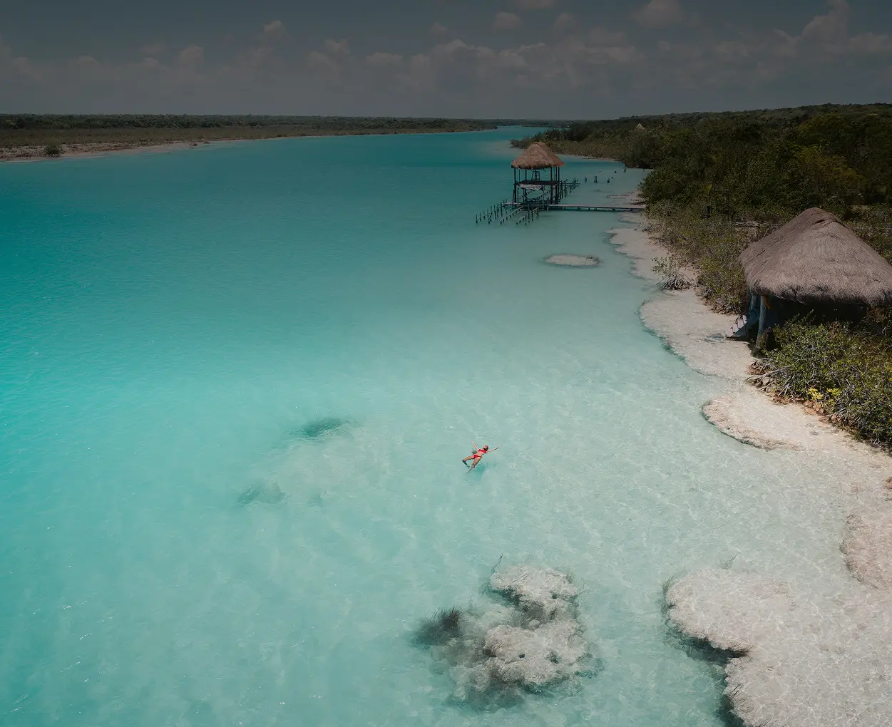 Person swimming in crystal-clear turquoise water near tropical huts